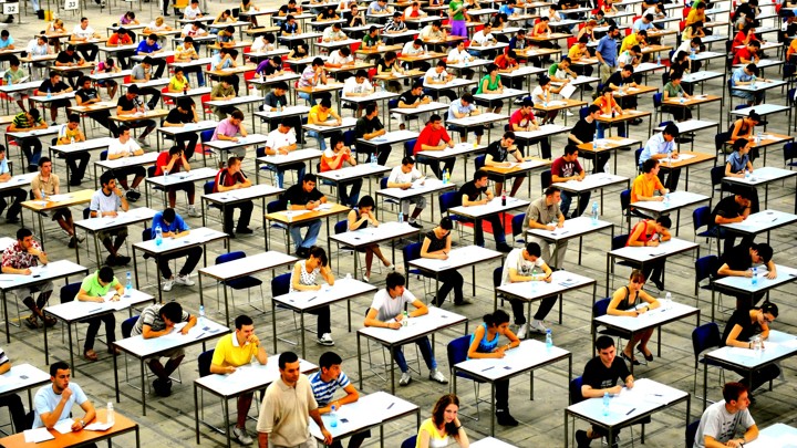 Picture of a large hall full of desks with students taking a test